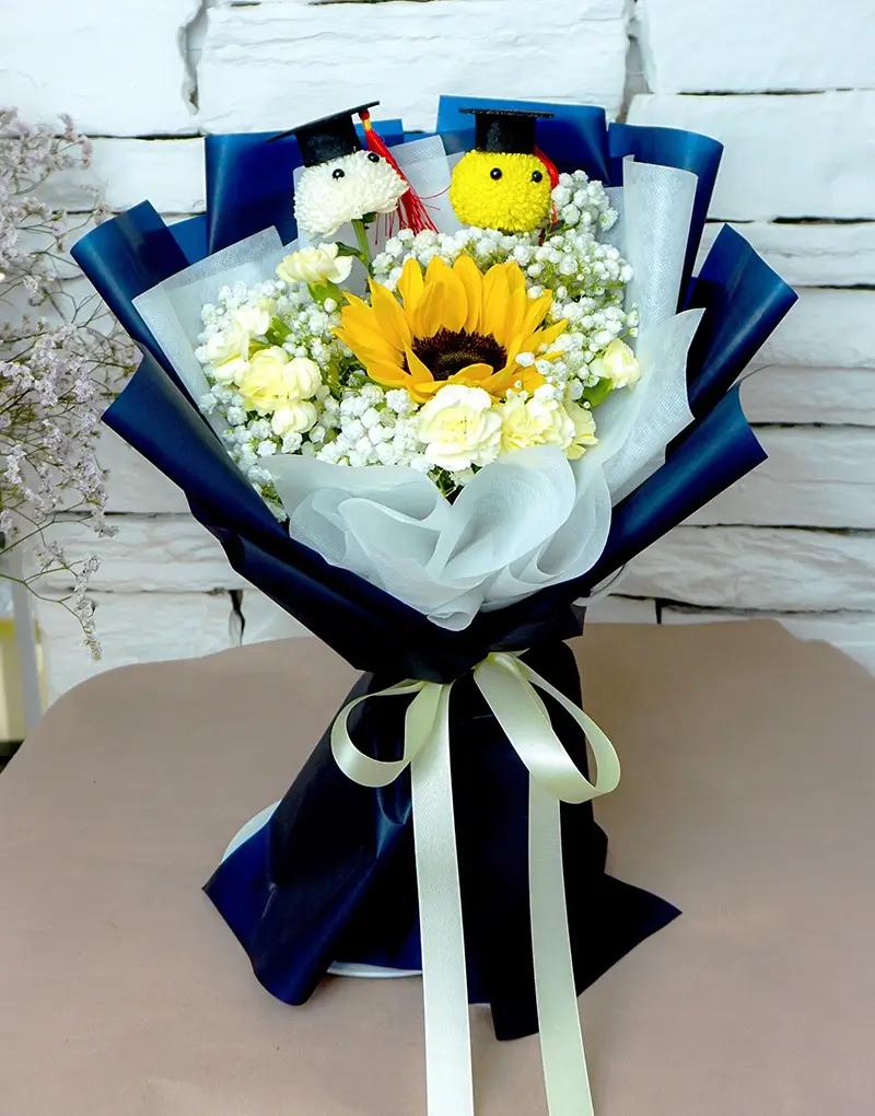 A391 graduate pom pom bouquet with a sunflower, spray carnations, and gypsophila.